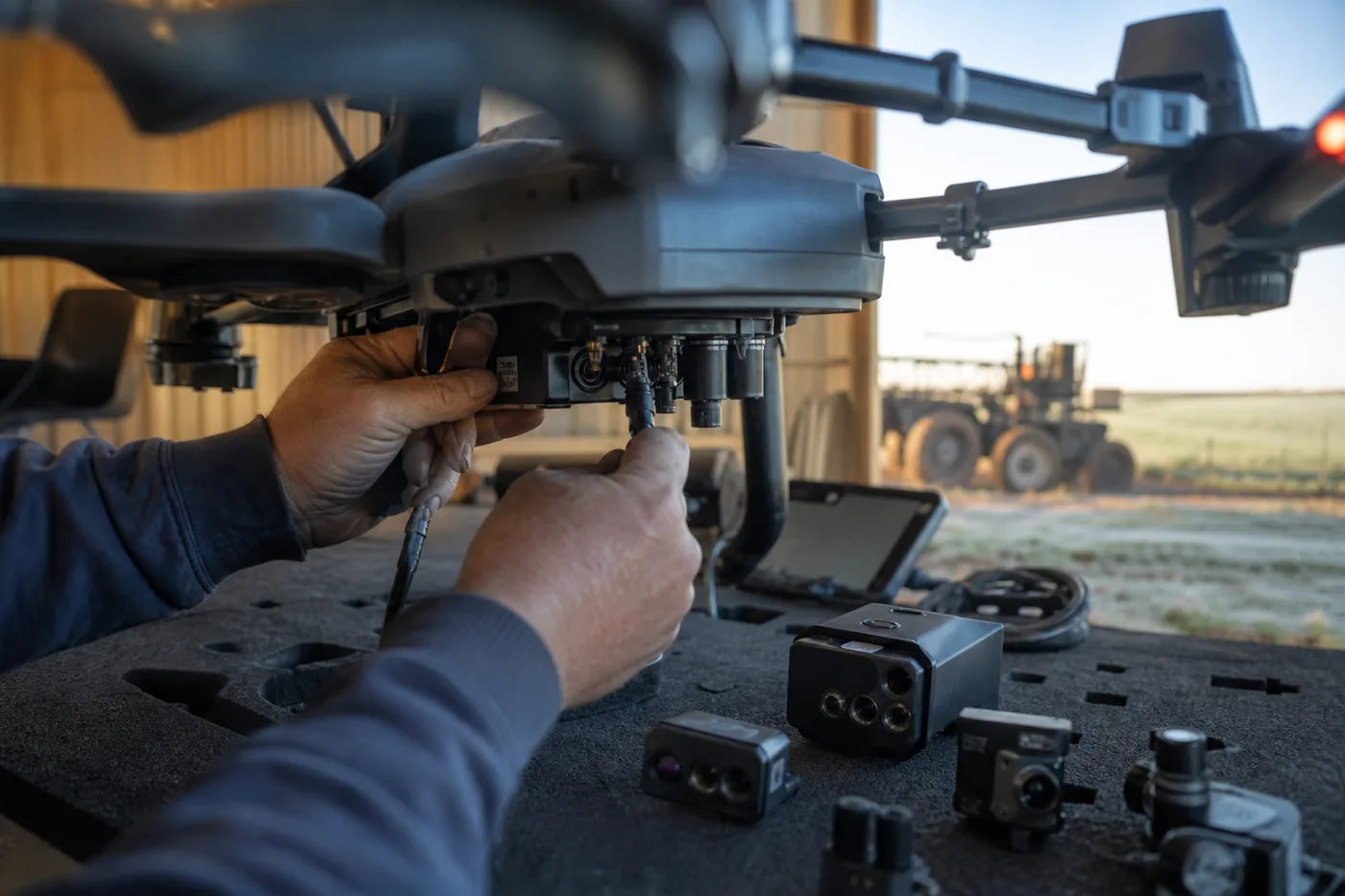 A person connects a cable into the underside of a large drone resting on a table.