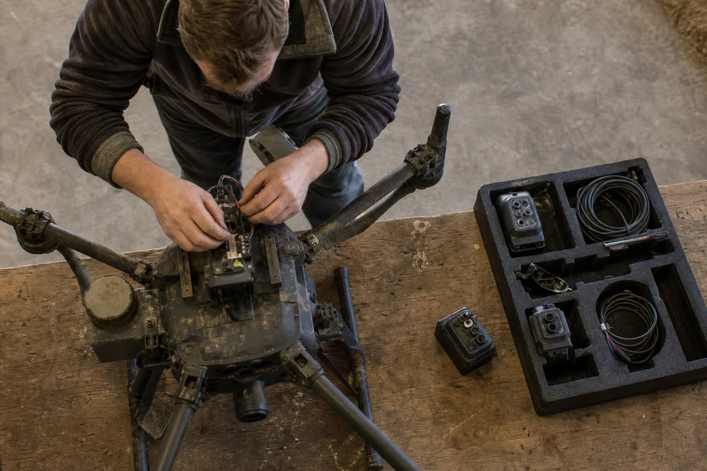 A person works on the wiring of a large drone on a wooden table.